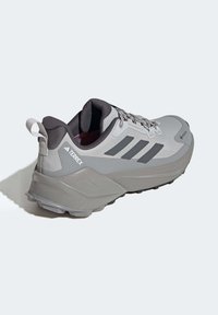 Grijze sportieve schoen met een gestructureerd bovenwerk, drie kenmerkende strepen, een gevoerde zool en een hieltab voor gemakkelijk aan- en uittrekken.
