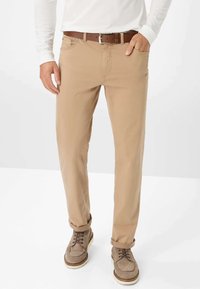 Beige Baumwollhose mit geradem Schnitt, ausgestattet mit einem braunen Ledergürtel und aufgerollten Säumen, ergänzt durch beiges Wildleder-Schuhwerk.
