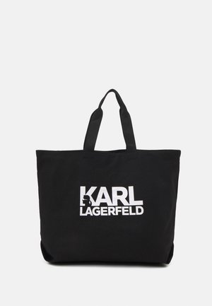 Czarna torba typu tote z podwójnymi uchwytami i białym napisem "KARL LAGERFELD", zawierająca małą stylizowaną sylwetkę w literze "K".