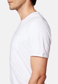 Biała koszulka z krótkim rękawem, z okrągłym dekoltem i kieszonką na lewej piersi. Wykonana z miękkiej bawełny, o gładkiej fakturze.