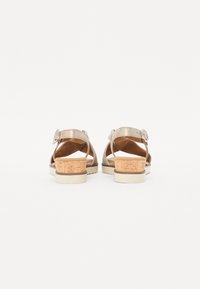 Sandales à talons beiges avec des accents en liège et une sangle dotée d'une boucle en métal. La semelle est de couleur claire avec une finition texturée.