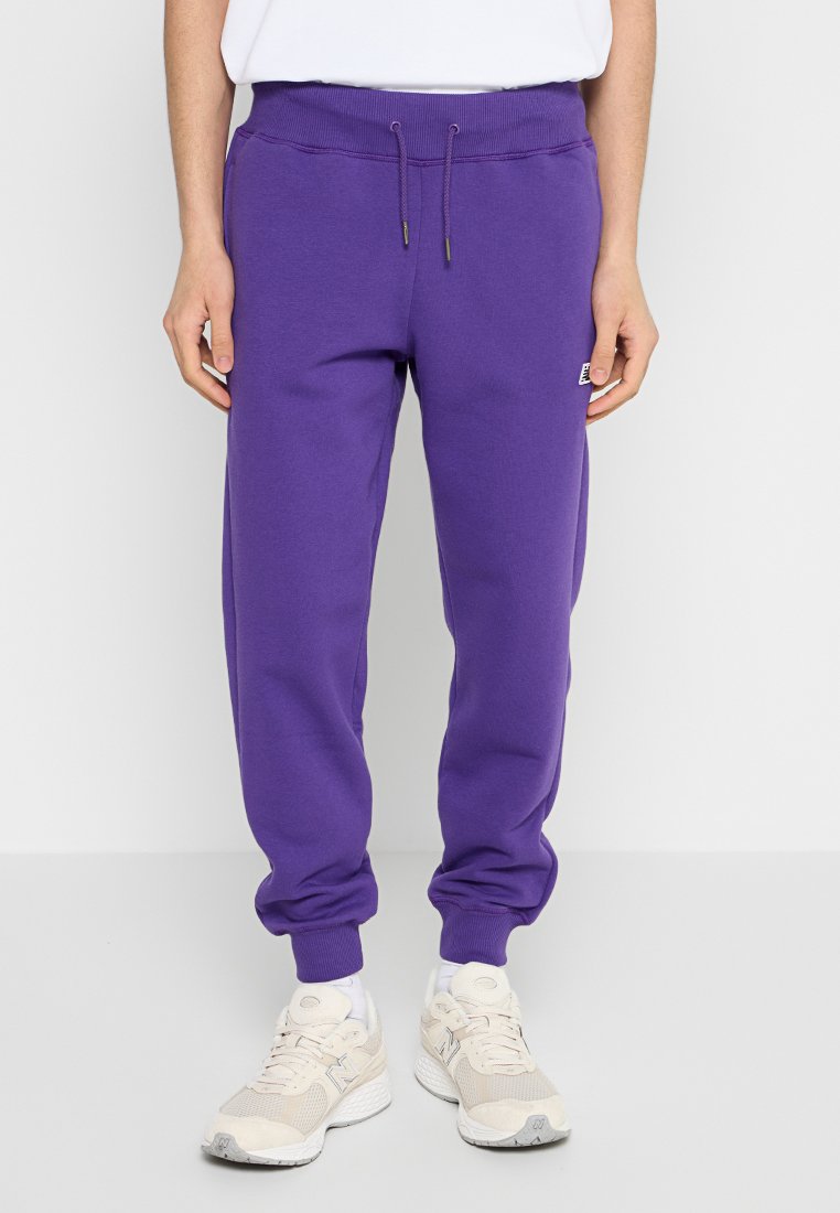 Pantaloni della tuta viola realizzati in un morbido tessuto misto cotone, con una vita regolabile tramite coulisse e polsini a costine. Presentano un'etichetta con il logo.