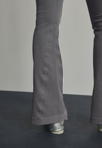 Pantaloni grigi a coste aderenti con una silhouette svasata, caratterizzati da una finitura testurizzata e abbinati a scarpe argento metallico.