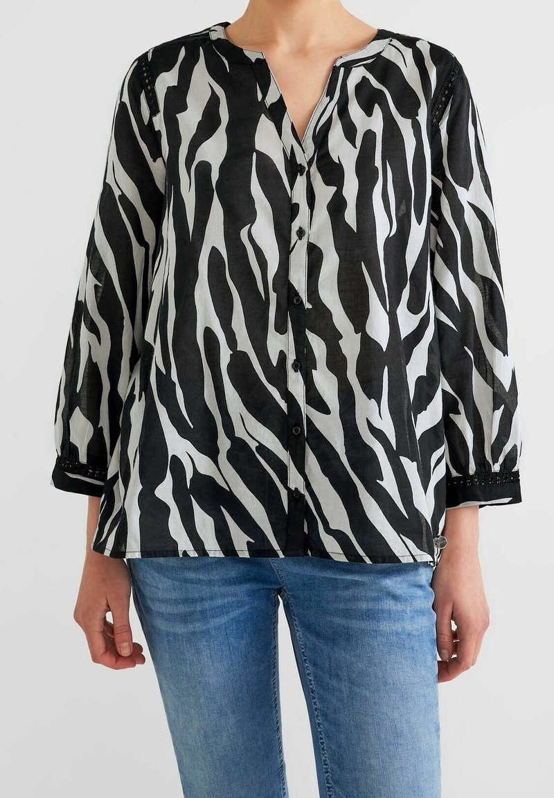 Camicia con stampa a zebre in bianco e nero, con scollatura a V, bottoncini davanti e maniche a tre quarti. Tessuto leggero e dalla texture con dettagli in pizzo.