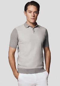 Szara koszulka polo z krótkim rękawem o teksturowanym wzorze, z kołnierzykiem i zapięciem na guziki. W zestawie z białymi spodniami z gładkiego materiału.