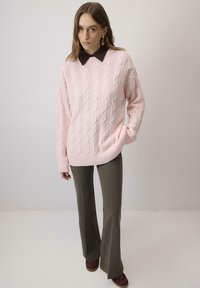 Pulover din fir gros tricotat, de culoare roz deschis, cu tiv ribotat, asortat cu pantaloni evazați de culoare măslinie și pantofi burgundy. Cămașă maro cu guler purtată dedesubt.