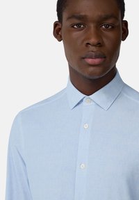 Camisa de botón azul claro hecha de una tela Texturada. Presenta un collar clásico y botones blancos, mostrando un patrón sutil.