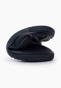 Zapato negro plegable con suela de goma texturizada, parte superior de cuero liso y una correa segura. Presenta un diseño compacto y curvado para un fácil almacenamiento.