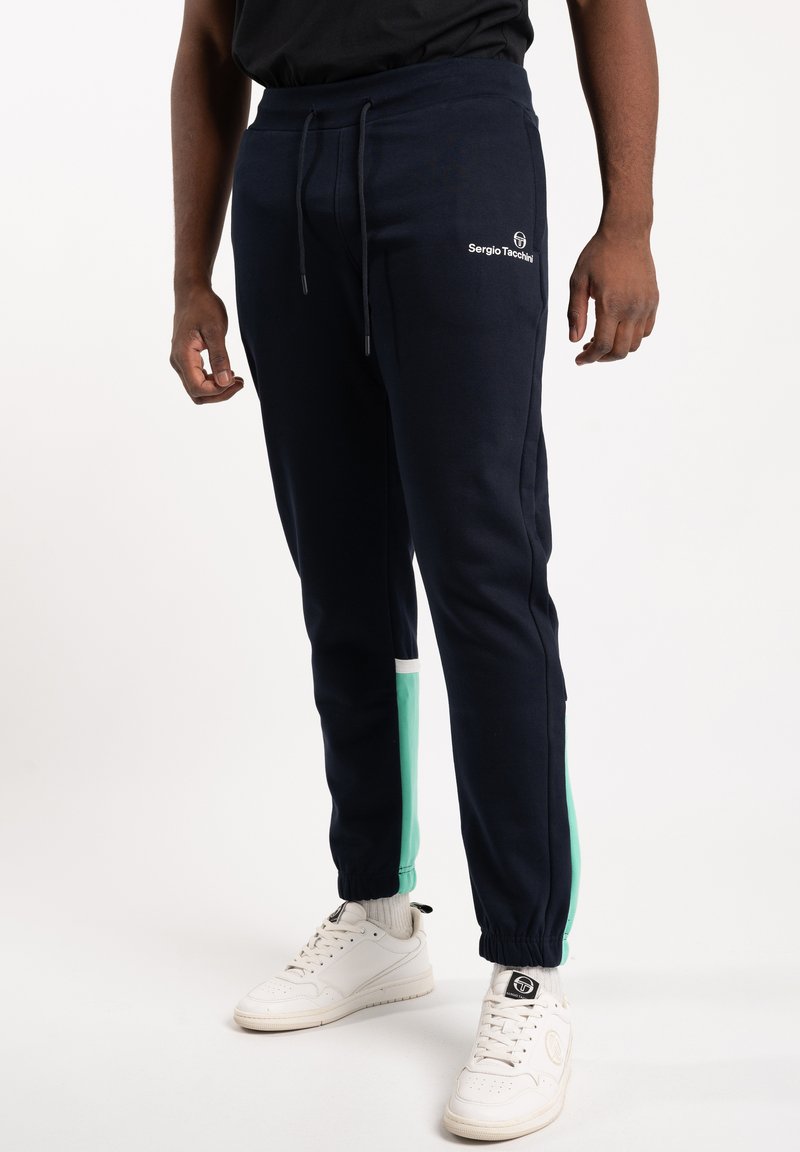 Marinblå sweatpants med gröna sidopaneler, accentuerad dragsko och logodetalj. Tillverkade av mjukt material, med elastiska muddar och fickor.