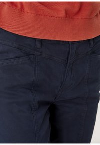 Granatowe spodnie wykonane z miękkiego materiału, z przeszytymi szwami i dopasowanym krojem. Pas ma lekko elastyczną strukturę dla większego komfortu.