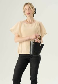 Zwarte neplederen emmer tas met gouden accenten, textuur van krokodillenpatroon, gecombineerd met een beige chiffon top en zwarte skinny jeans.