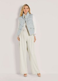 Hellblau gepolsterte Weste über einem weißen gerippten Oberteil, kombiniert mit weit geschnittenen cremefarbenen Hosen. Weiche Texturen und neutrale Farben dominieren das Outfit.