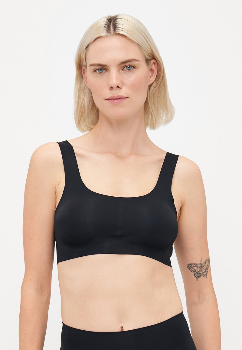 Svart bh med brede stropper og scoop-hals. Laget av glatt, elastisk stoff, har den et sømløst design og minimalistisk stil.