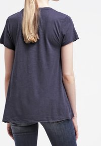 Námořnické tričko s krátkým rukávem vyrobené z lehké tkaniny s volným střihem, s kulatým výstřihem a syrovými detaily na zadním lemu.