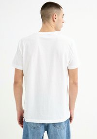 Camiseta blanca de manga corta hecha de algodón suave. Presenta un cuello redondo y un dobladillo recto, combinada con unos vaqueros de color azul claro.