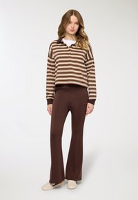 Maglione a righe con colletto, con tonalità marroni e crema; abbinato a pantaloni marroni aderenti a zampa e sneakers di colore chiaro.