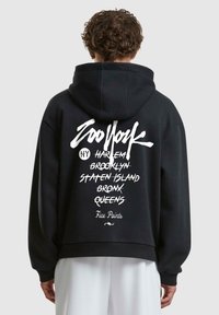 Schwarzer Kapuzenpullover mit einem weißen grafischen Design auf dem Rücken, das verschiedene New Yorker Orte in einer Mischung aus Kursiv- und Fettdruck auflistet.
