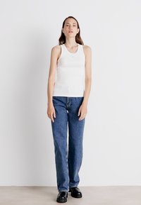 White fitted tank top, blue high-waisted jeans, and black shoes. Simple, sleeveless design with a rounded neckline. Smooth texture and casual fit.