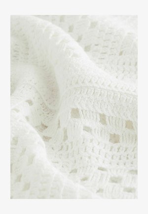 Weiß gestrickte Decke mit offenem, gemustertem Muster aus weichem, grobem Garn. Sie wirkt gemütlich und einladend.