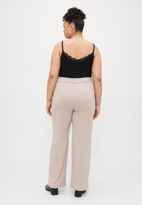 Svart cami med blonder, beige vide bukser med elastisk midjebånd, og svarte hæles ankle støvler. Enkle bakgrunn.