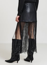Schwarzer Minirock aus Leder mit Fransen-Overlay. Verfügt über eine taillierte Passform, vertikale Fransenverzierung und schlanke, spitze schwarze Stiefel.
