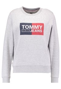 Felpa grigia chiara con maniche lunghe, collo a giro e logo "TOMMY JEANS" in lettere bianche su uno sfondo rettangolare blu navy e rosso.