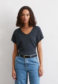 T-shirt grigio scuro a V con maniche corte, realizzato in un tessuto texturizzato, indossato con jeans blu in denim a vita alta e una cintura nera.