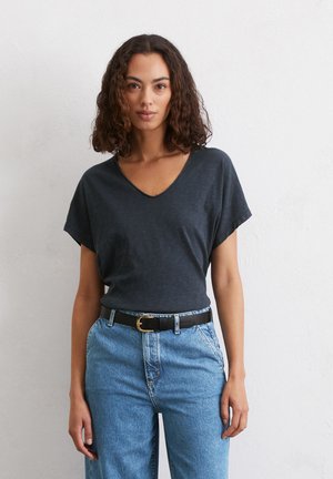 Czarna, szara koszulka V-neck z krótkimi rękawami, wykonana z teksturowanej tkaniny, noszona z niebieskimi dżinsami o wysokim stanie i czarnym paskiem.