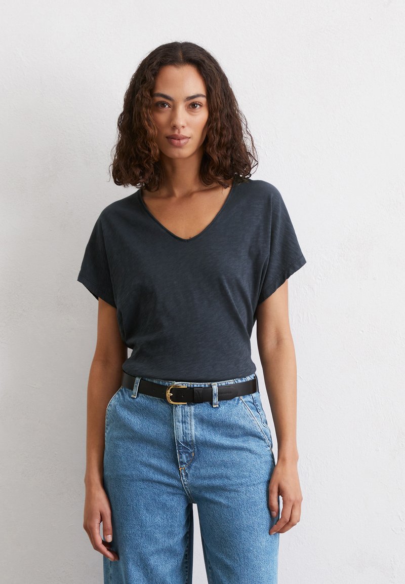 T-shirt grigio scuro a V con maniche corte, realizzato in un tessuto texturizzato, indossato con jeans blu in denim a vita alta e una cintura nera.