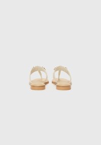 Sandales blanches à bout ouvert avec une semelle plate de couleur brun clair, comportant deux brides et un matériel décoratif sur le côté. Design simple et texture lisse.