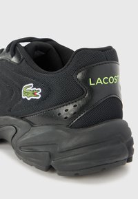 Black athletic shoe featuring mesh and leather materials, rubber sole, green "LACOSTE" logo, and embroidered crocodile detail.