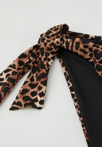 Nahaufnahme eines Leopardenmuster-Bikinihöschen mit einer Stoffschleife auf der linken Seite vor einfachem Hintergrund.