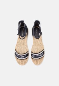 Granatowe espadryle z tkaniny z plecionymi podeszwami. Posiadają czarno-białe paski z logo "TOMMY HILFIGER". Otwarty tył z akcentami klamrowymi.