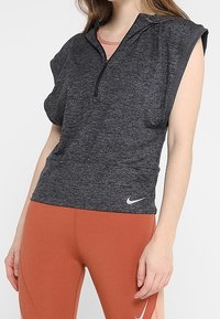 Kortärmad, zip-up träningsöverdel i mörkgrått tyg med mjuk textur. Har huva och en liten vit logotyp på fållen.