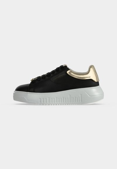 Μαύρο χαμηλό sneaker με παχιά λευκή σόλα και μεταλλικό χρυσό λεπτομέρεια στη φτέρνα, με μαύρα κορδόνια και διακριτικό πλευρικό λογότυπο.