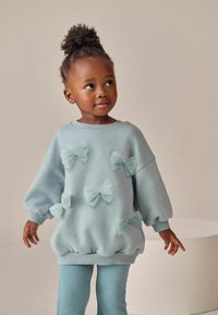 Lys blå sweatshirt med puffede ærmer, der har flere gennemsigtige sløjfer. Sammen med matchende ribbede blå leggings for et koordineret look.