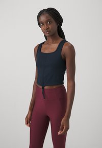 Námornícky crop top s hranatým výstrihom a nastaviteľným šnúrkovým detailom, skombinovaný s vysoko pásovými vínovými legínami. Hladká, elastická látka.