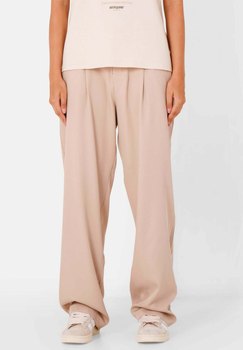 Beige wijde broek met plooien, gemaakt van lichtgewicht stof, gecombineerd met beige sneakers. Eenvoudige, ontspannen pasvorm met een zachte textuur.