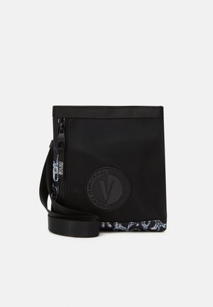 Sac bandoulière noir avec un logo rond embossé Versace Jeans Couture, fermeture éclair sur le côté et bordure à motif en bas.