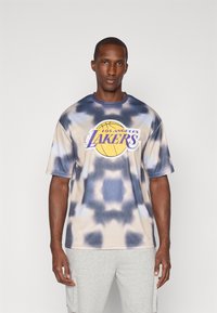 Kortærmet tie-dye T-shirt i beige og blå med et cirkulært gult og lilla "Los Angeles Lakers" logo på forsiden.