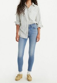 Camisa blanca con rayas verticales azul marino, mangas remangadas; pantalones pitillo azul claro; zapatos beige estilo mocasín.