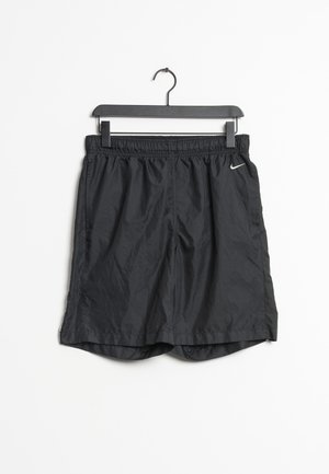 Mustat Nike-urheilushortsit, joissa on joustava vyötärönauha, roikkuvat mustassa muovisetissä valkoista taustaa vasten.