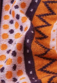 Dzianina z wzorami powtarzających się pomarańczowych i fioletowych kropek na jasnoróżowym tle, z zygzakowymi i geometrycznymi wzorami.