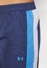 Námorné šortky so bočnými panelmi v svetlom modrom a bielom, vyrobené z ľahkej tkaniny. Majú elastický pás a logo Under Armour.