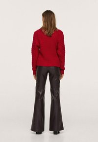Pullover rosso lavorato a maglia con motivi testurizzati, abbinato a pantaloni neri in pelle a vita alta e svasati. La vista posteriore mostra l'orlo e le maniche a coste.