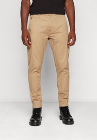 Kakhi chinos slim kroja, izdelani iz bombaža, z bočnimi žepi in zadrgo. Obuti z črnimi čipkastimi škornji.