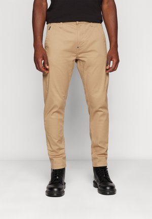 Kakhi chinos slim kroja, izdelani iz bombaža, z bočnimi žepi in zadrgo. Obuti z črnimi čipkastimi škornji.