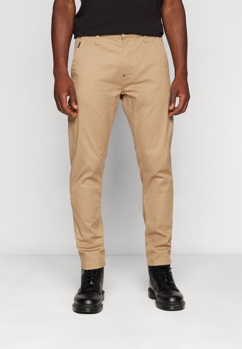 Kakhi chinos slim kroja, izdelani iz bombaža, z bočnimi žepi in zadrgo. Obuti z črnimi čipkastimi škornji.