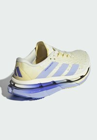 Scarpa da corsa in giallo e viola con una tomaia testurizzata, design a tre strisce, una suola spessa con un colore sfumato e dettagli di marca.