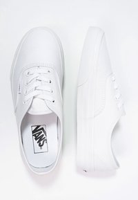 Baskets basses en toile blanches Vans avec lacets à l’avant, semelle plate et logo visible sur la semelle intérieure, vues de dessus et de côté.